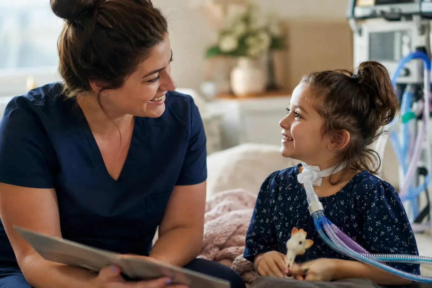 A nurse reads a picture book with a young girl who has a tracheostomy and ventilator tubing.